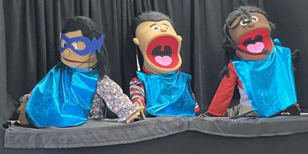 Three puppets wearing capes